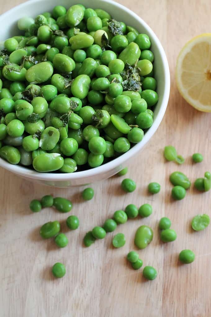 broad bean and pea salad in a white bowl with a halved lemon in the background