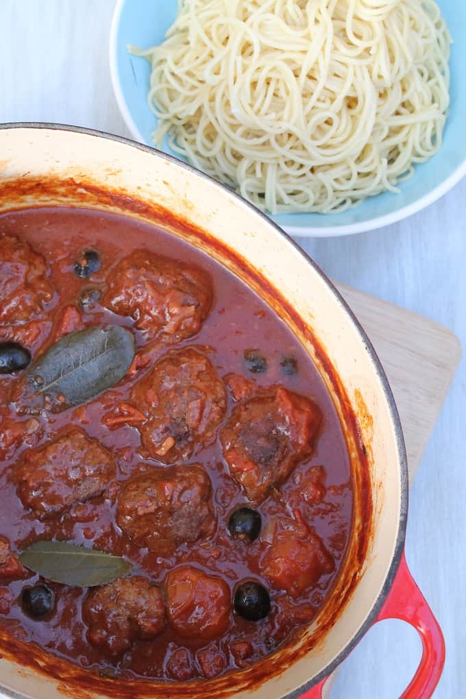 Meatballs in Chorizo & Black Olive Sauce in a large ovenproof dish with a bowl of spaghetti in the background