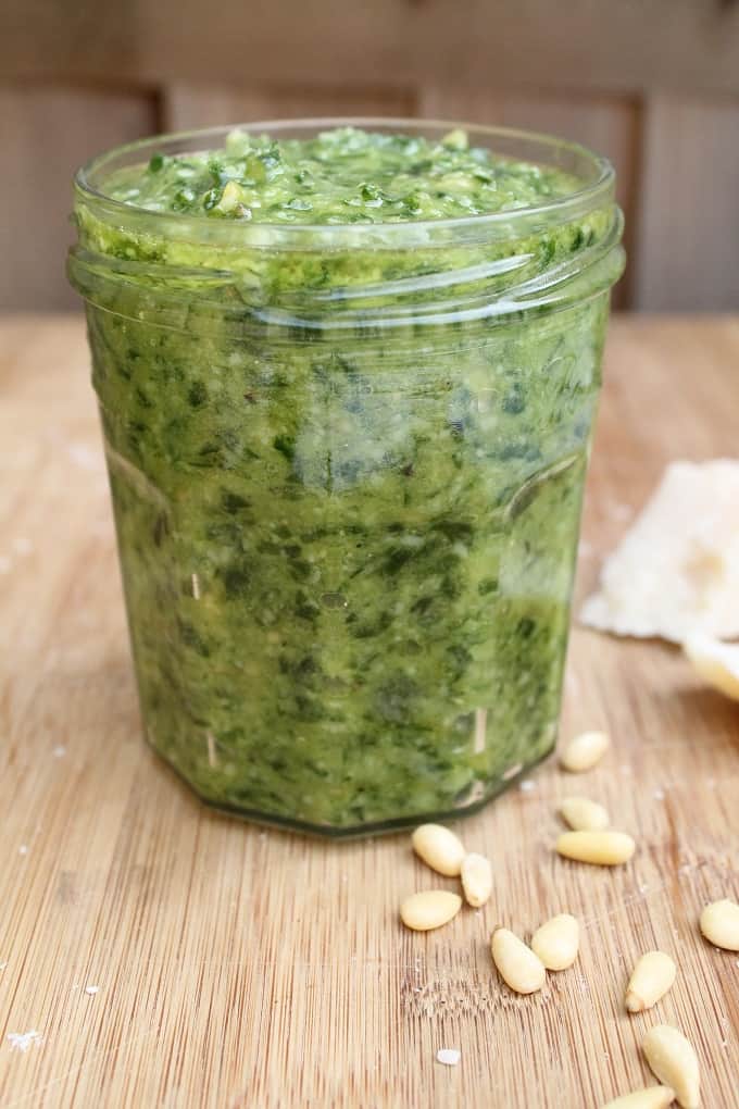 wild garlic pesto in a glass jar with pine nuts scattered in the foreground