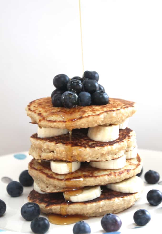 healthy oat pancakes piled up with sliced banana and blueberries, drizzled with honey