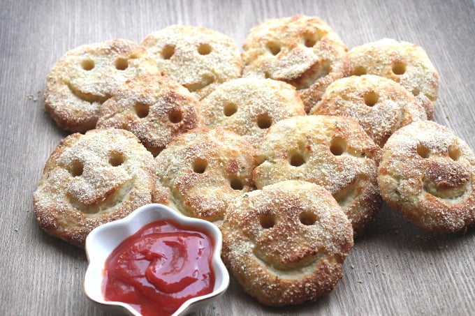 homemade potato smiles with a small white bowl of tomato ketchup in the foreground.