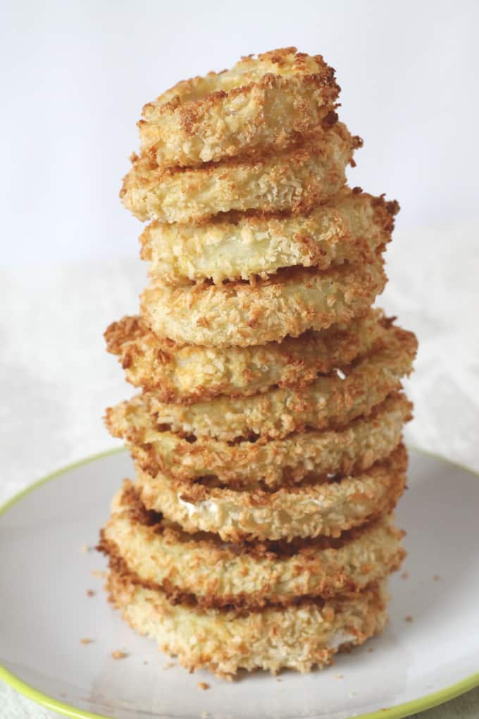 baked onion rings stacked in a tower on a white plate with a green rim