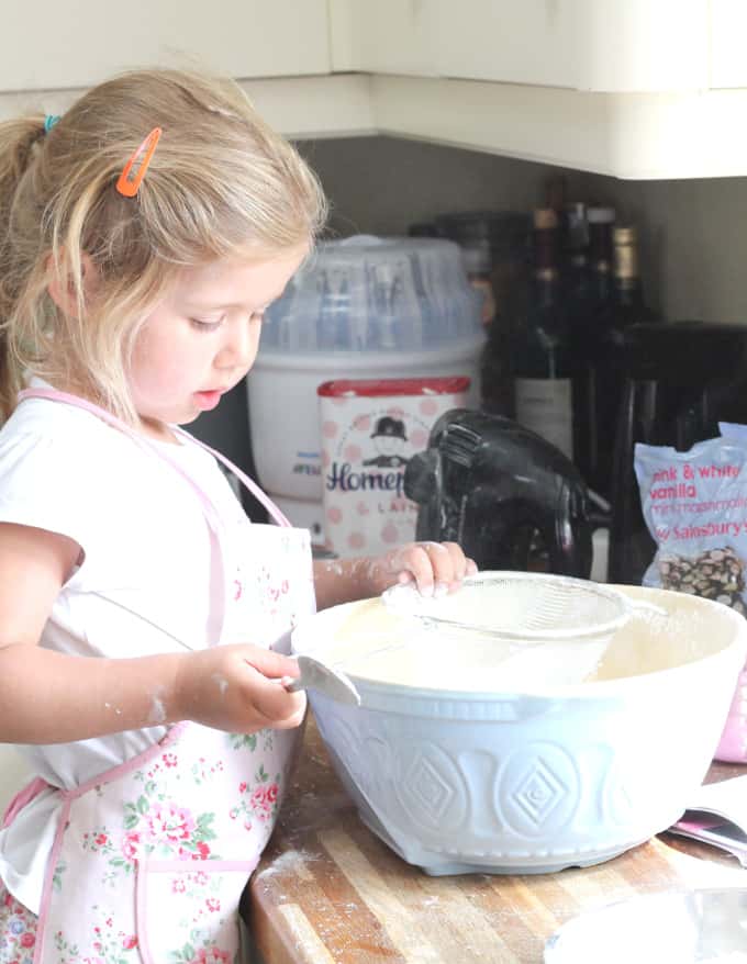 a small child sifting flour into a large blue baking bowl