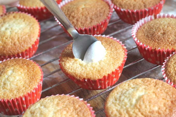 marshmallow fluff being spooned into the hole in the cupcake