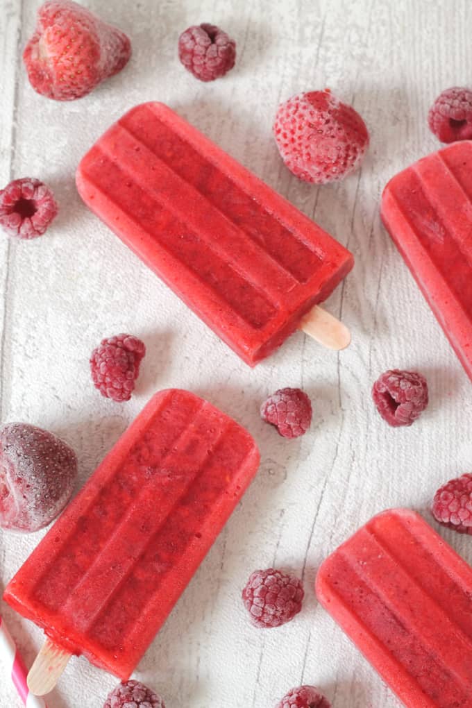 10 calorie popsicles on a white wooden board surrounded with frozen red berries