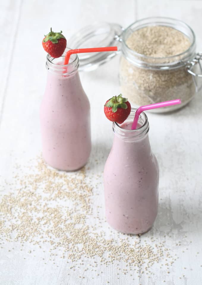 two quinoa smoothies in glass milk bottles with a strawberry on the rim of each of the bottles and a straw in each