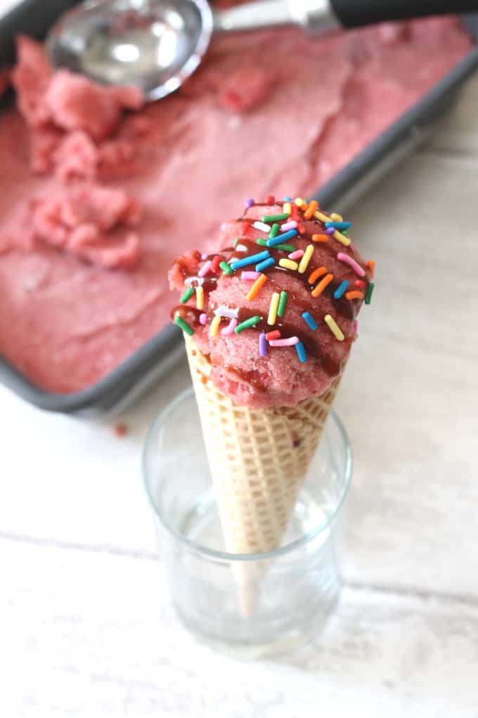 Two Ingredient Healthy Strawberry Ice Cream  served in an ice cream cone and decorated with multi coloured sprinkles.