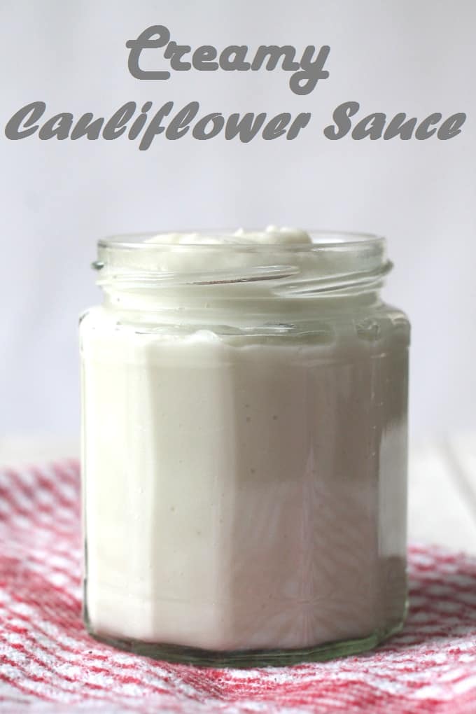 creamy cauliflower sauce in a glass jar sitting on top of a red gingham cloth