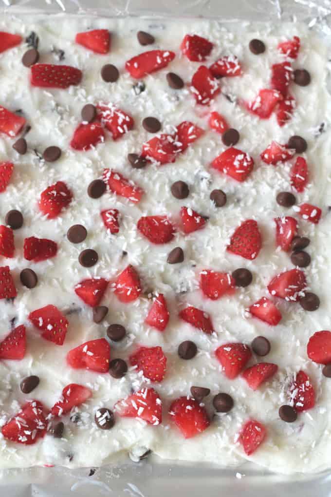 a tray of frozen yogurt bark topped with strawberries, chocolate chips and coconut flakes.