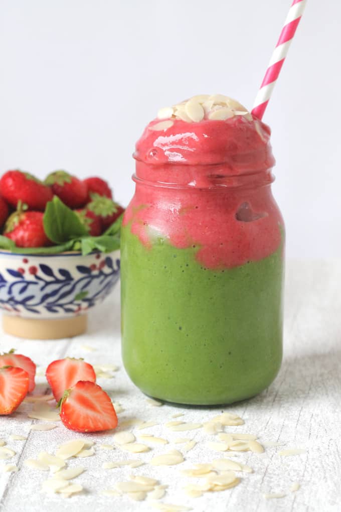 frozen superhero smoothie layered in a glass jar, topped with almond flakes and a blue and red stripy straw