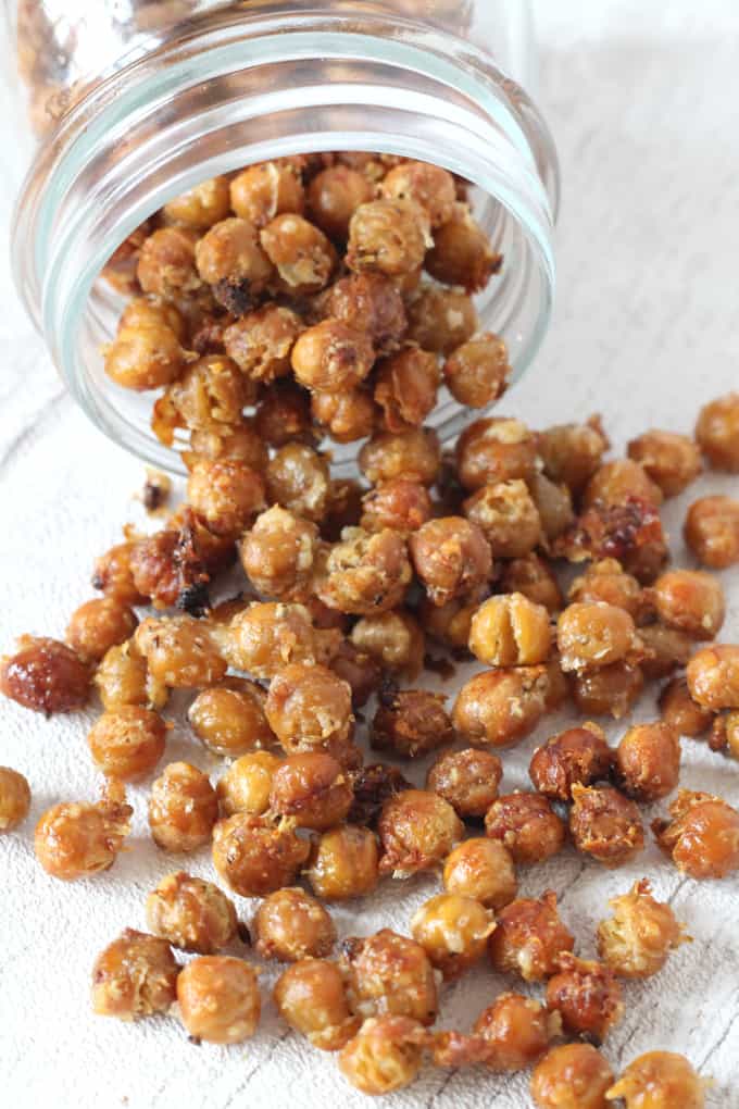 roasted chickpeas falling out of a glass jar onto a white wooden chopping board