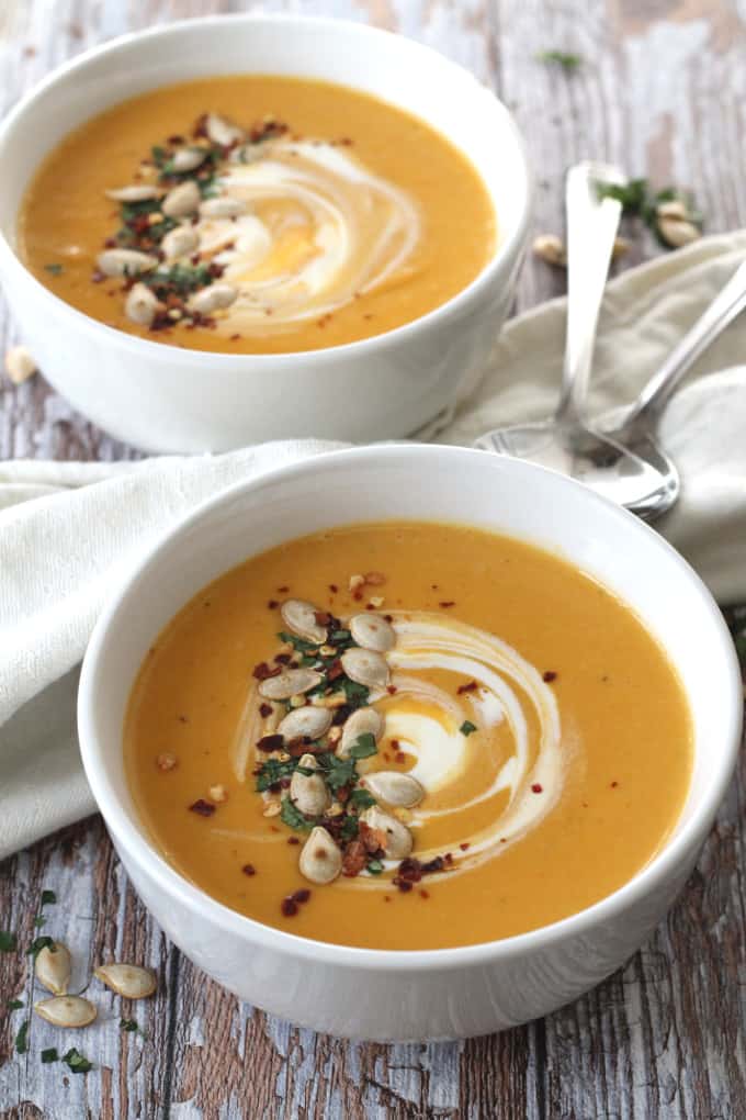 Two bowls of Spiced butternut squash soup topped with pumpkin seeds, chilli flakes and creme fraiche.