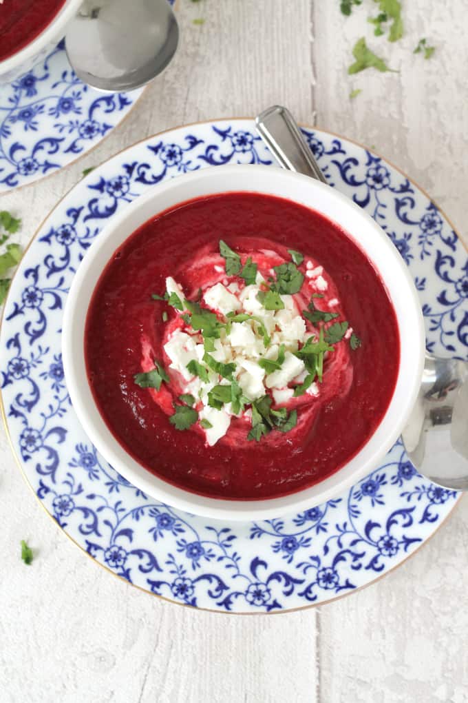 Beetroot and Carrot soup served in a white bowl on a blue and white side plate.