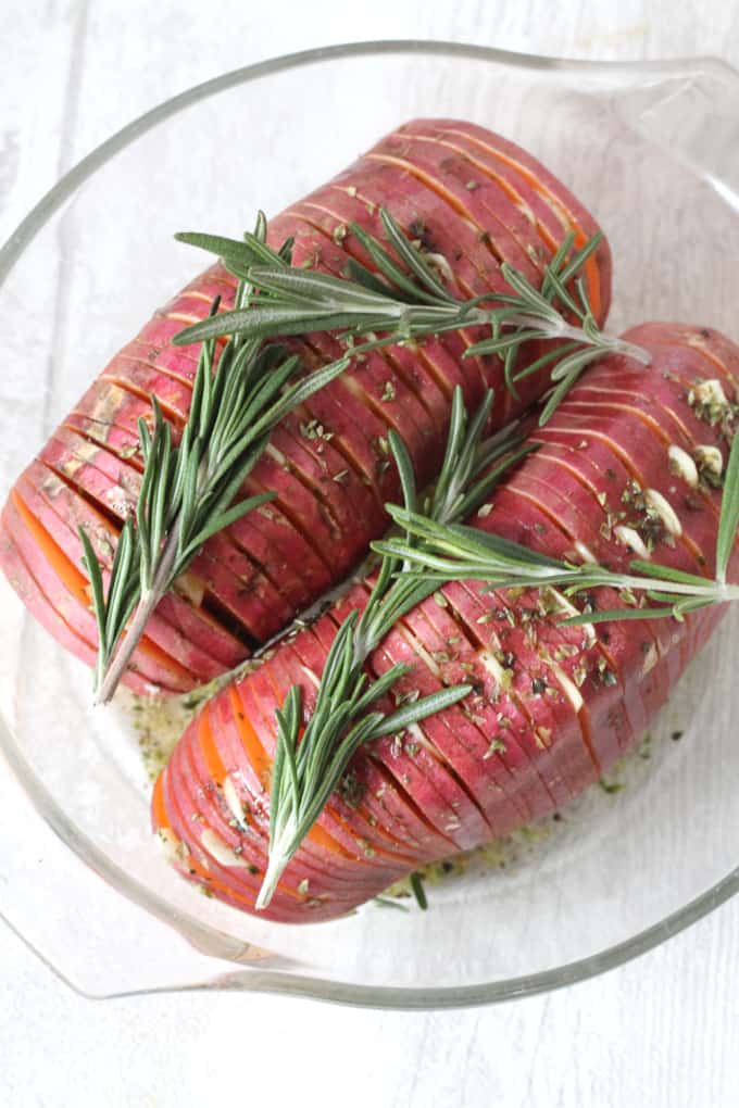 hasselback sweet potato topped with sprigs of rosemary, garlic and herbs