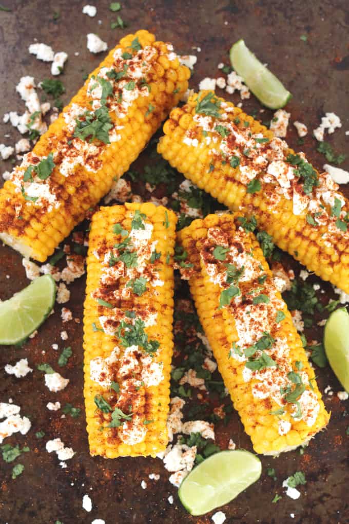 mexican corn on the cob with feta with lime quarters on a dark background