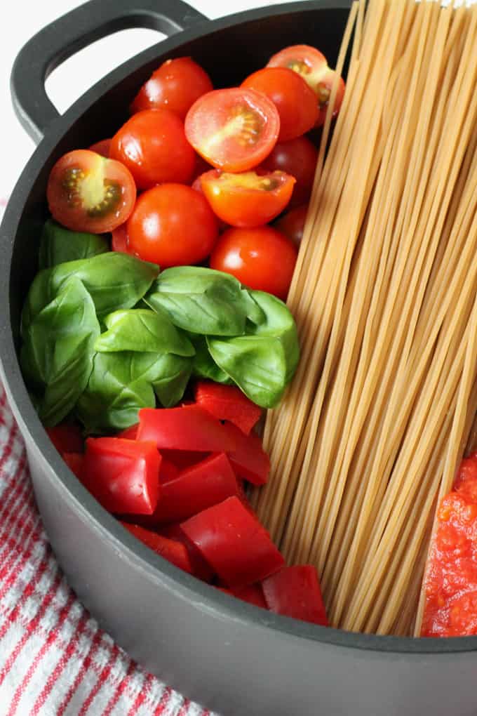 chopped cherry tomatoes, fresh basil leaves, gluten free pasta and chopped red peppers in a black pot