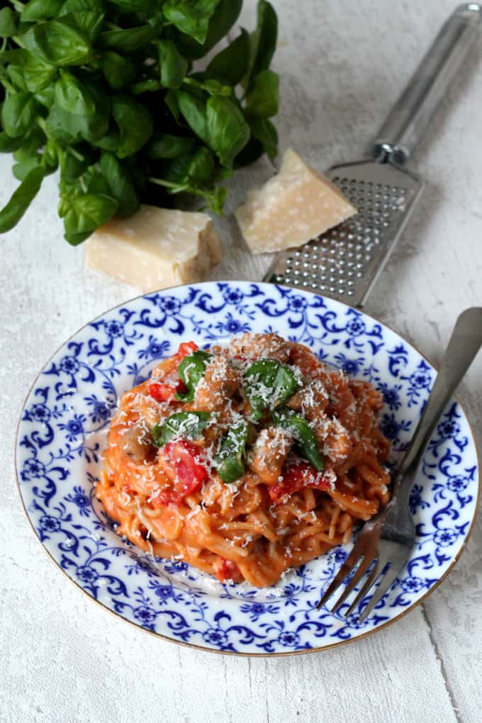 One Pot Creamy Sausage & Tomato Spaghetti served on a blue and white plate with grated parmesan and basil leaves