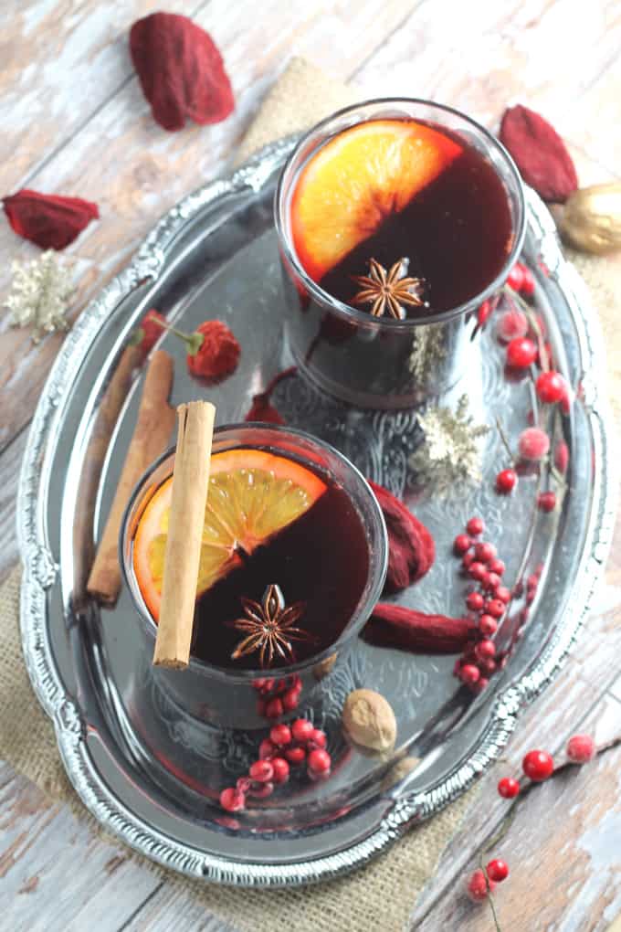 two glasses of paleo mulled wine served on a silver tray decorated with winter berries and nuts
