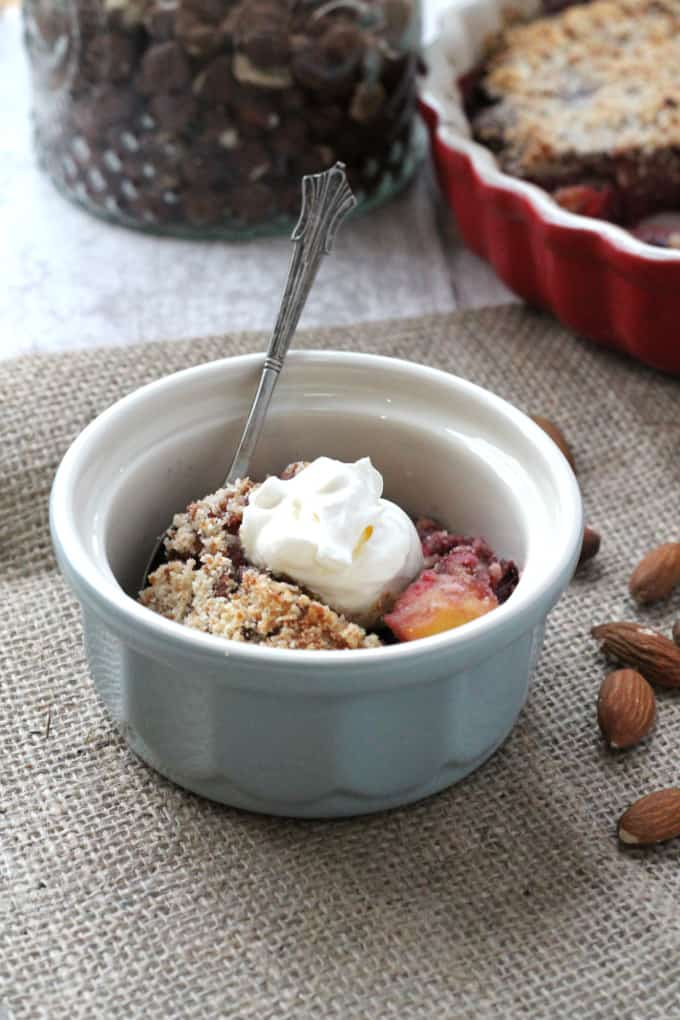 a small portion of the nutty winter crumble in a blue ramekin dish topped with a dollop of creme fraiche