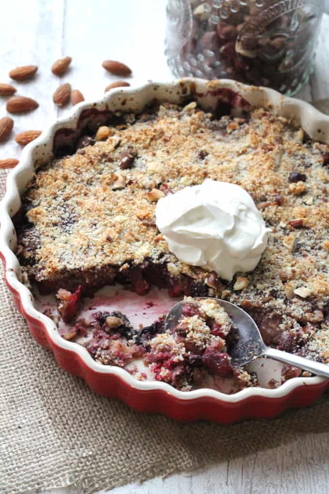 no grain berry apple crumble in a red ovenproof dish with a dollop of cream on top