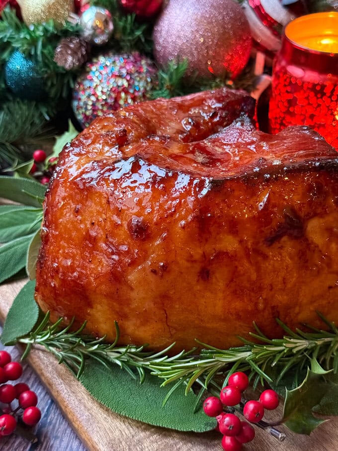 Slow Cooker Christmas ham sitting on a wooden chopping board on a bed of festive decor.