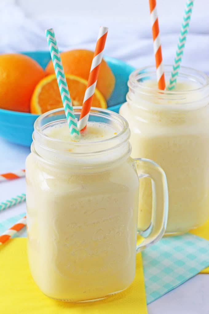 Creamy Orange Smoothie with orange and blue straws and whole oranges in the background