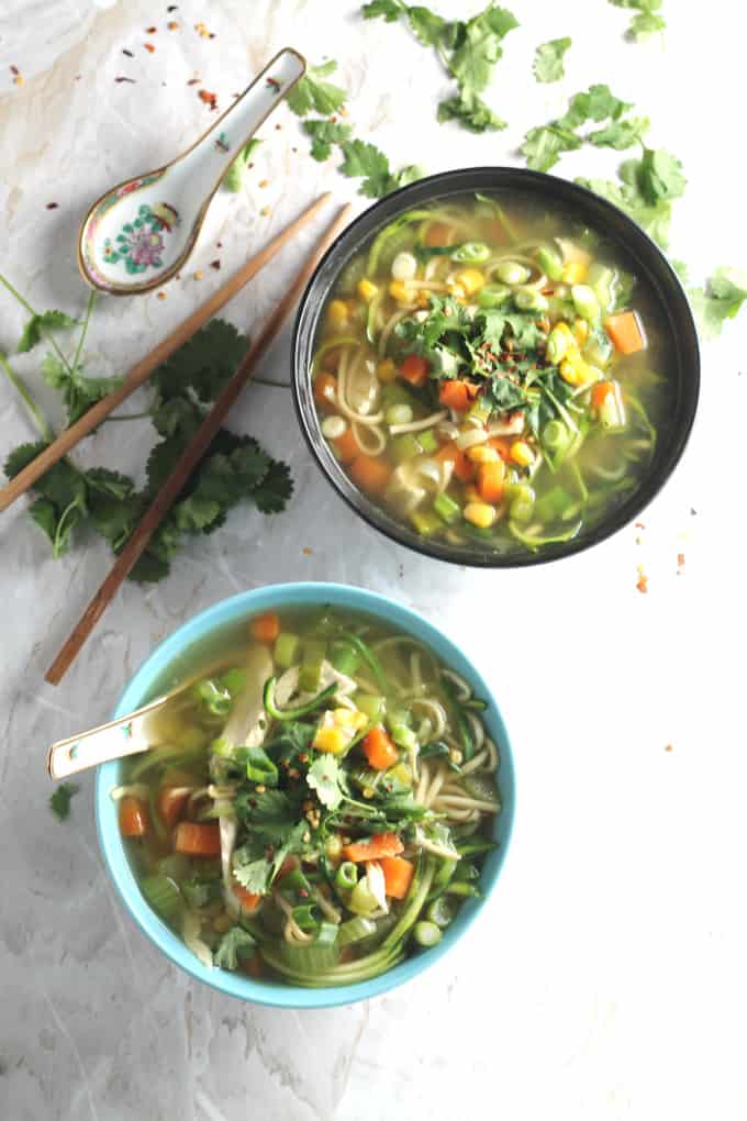 Two bowls of Chicken noodle zoodle soup with a set of chopsticks and an oriental soup spoon in the background.