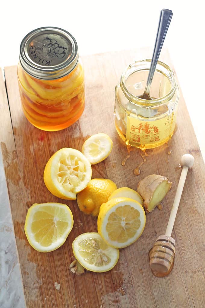 a jar of honey lemon ginger jar cold and flu remedy on a wooden chopping board with a jar of honey and some chopped and squeezed lemons