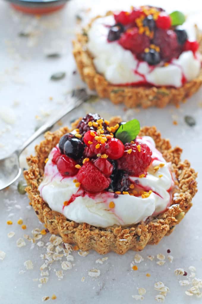 2 Granola Crust Breakfast Tarts filled with yogurt and berries on a marble background with a spoon