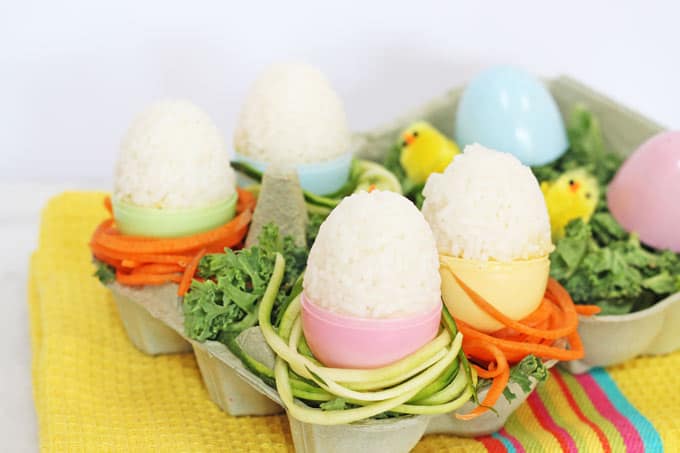 Healthy Rice & Veggie Easter Eggs in an egg carton, decorated with spiralized veggies and mini easter chicks