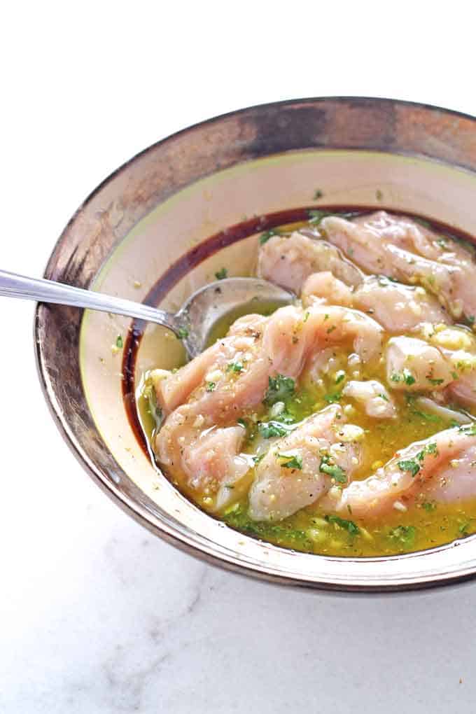 raw chicken pieces marinating in a bowl with a spoon in it