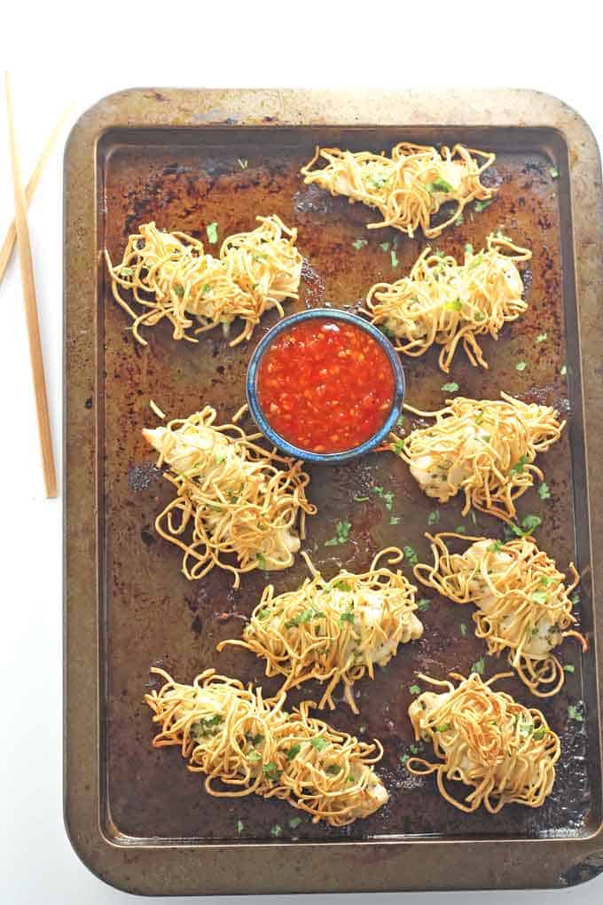 noodle wrapped chicken on a baking tray with a small blue pot of sweet chilli sauce