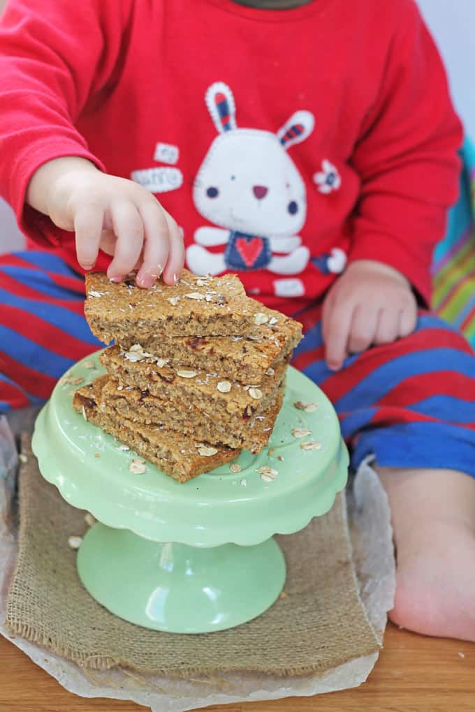 a small child picking up a slice of flapjack from a pile on a green cake stand