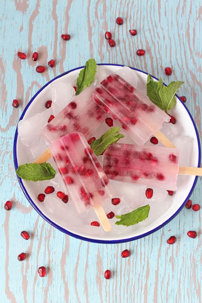 4 Pomegranate and Coconut Water Popsicles served in a bowl on top of ice sprinkled with pomegranate seeds and mint leaves