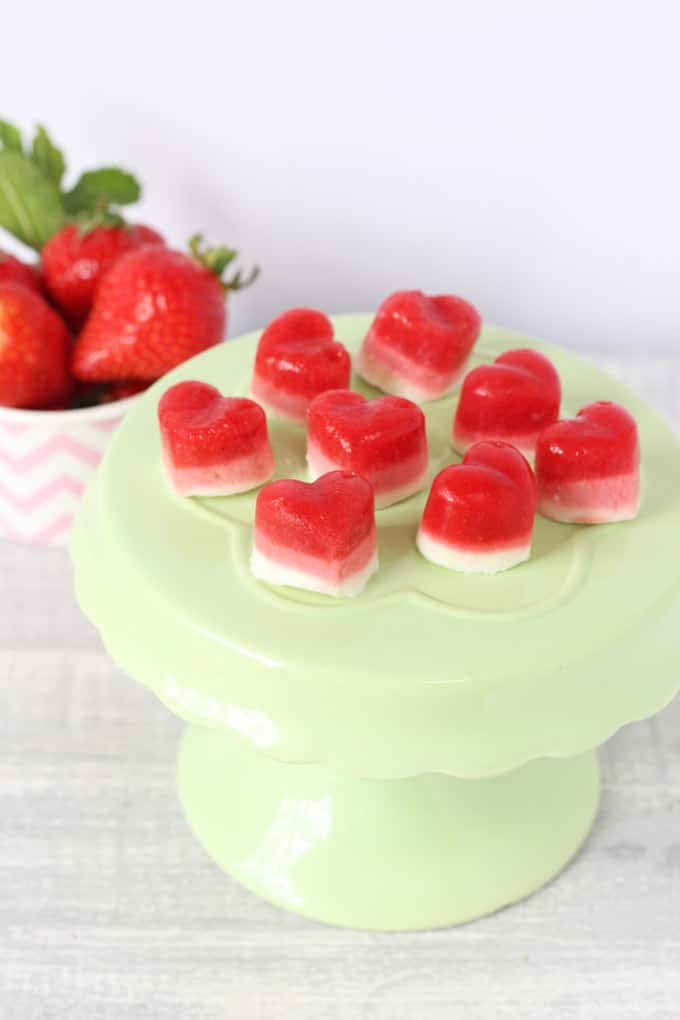 Strawberry Frozen Yogurt Bites on a green cake stand with a bowl of strawberries in the background