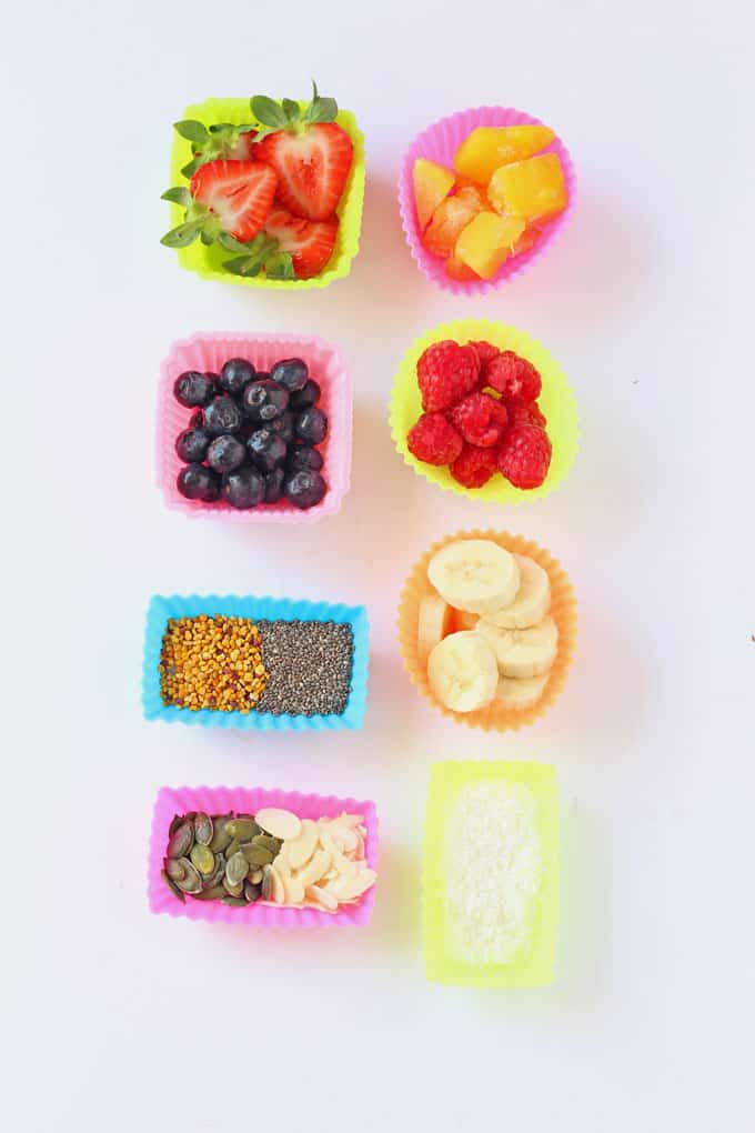 a selection of multi coloured silicone muffins cases filled with various nuts, seeds and berries