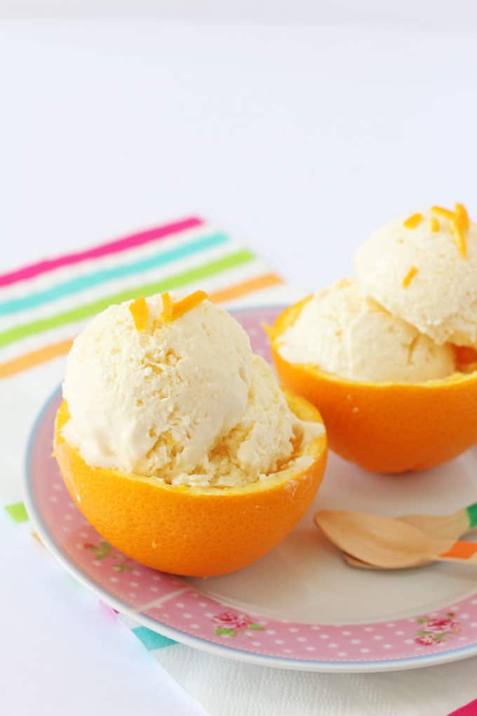 Orange frozen yogurt served in two orange halves on a pink polka dot plate