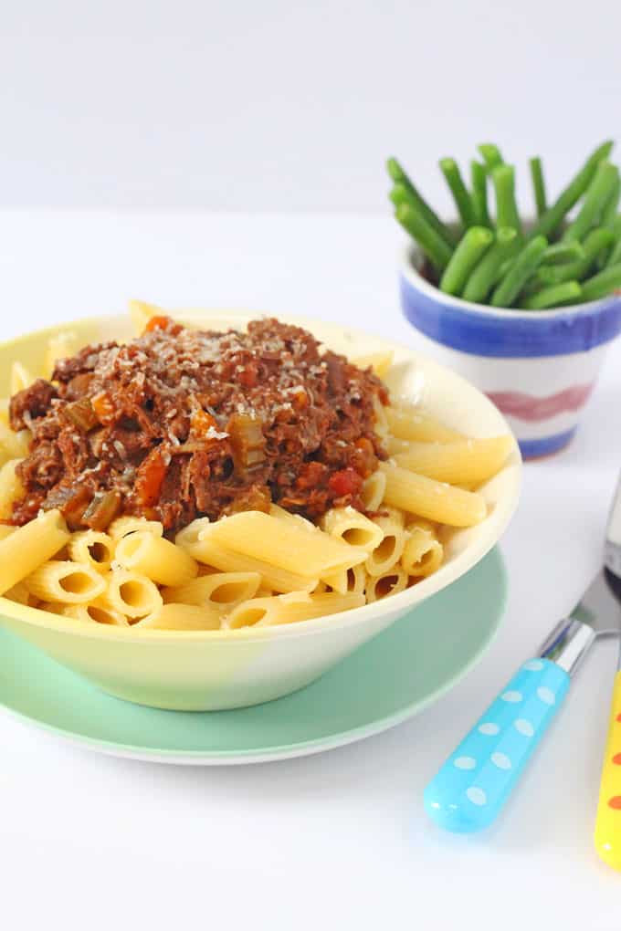 slow cooker ragu for kids served with pasta in white bowl and garnished with grated parmesan