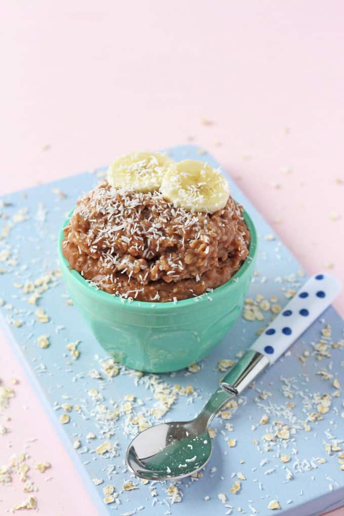 Chocolate & Coconut Porridge or Oatmeal served in a small turquoise bowl on top of a blue chopping board and next to a blue polka dot spoon.