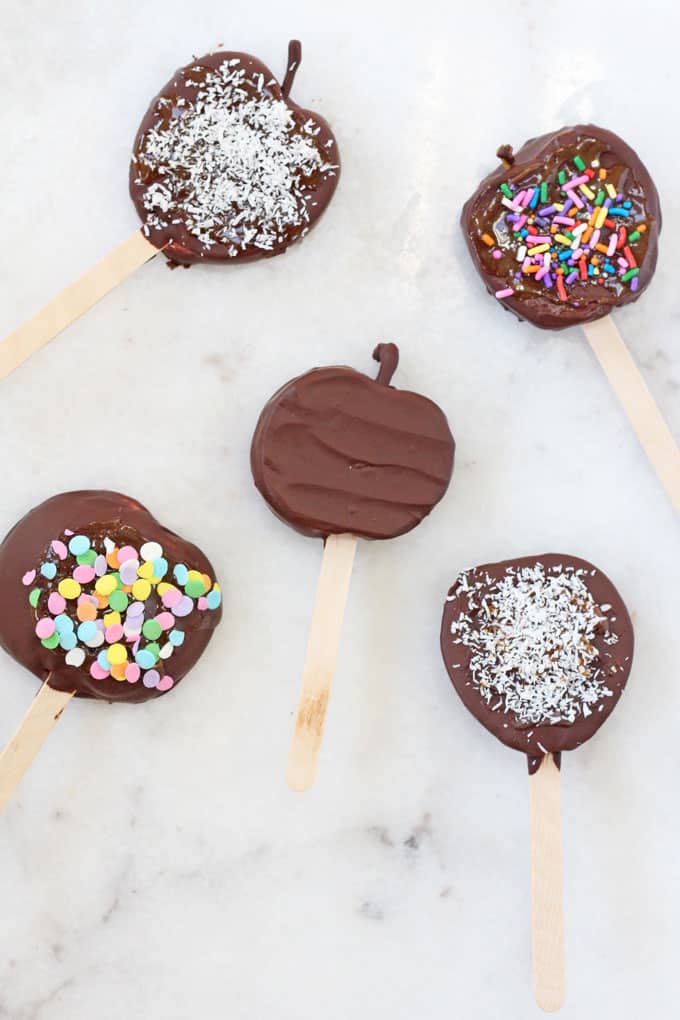 Five chocolate toffee apple slices decorated with various designs and toppings