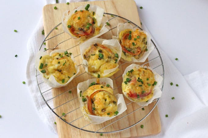Bacon, Cheese & Chive Egg Muffins on a wire cooling rack on top of a wooden chopping board. Garnished with chopped chives.