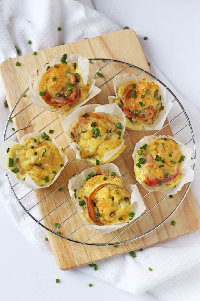 6 Bacon, cheese & chive egg muffins on a wire cooling rack on top of a wooden chopping board