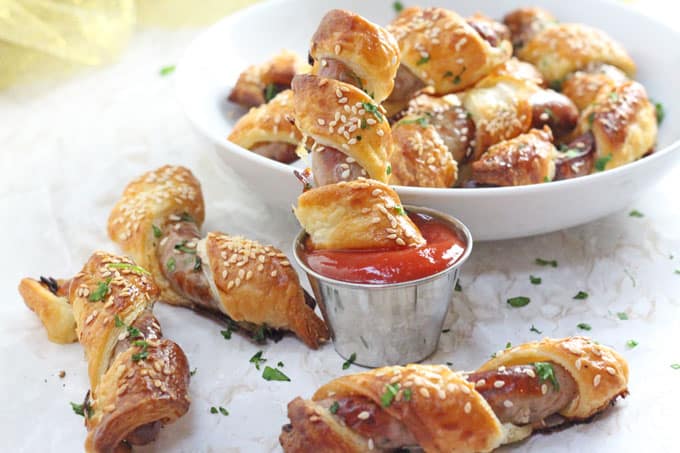 Cheat's Sausage Rolls served in a white bowl with a small pot of tomato sauce and garnished with green herbs