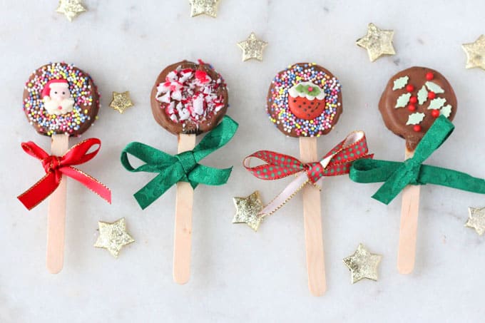 Four Christmas Oreo Pops are coated in chocolate and decorated with Christmas sprinkles and icing decorations. Tied with Christmas ribbon.