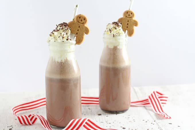 frozen gingerbread hot chocolate served in small glass bottles and topped with whipped cream, chocolate sprinkles and mini gingerbread men