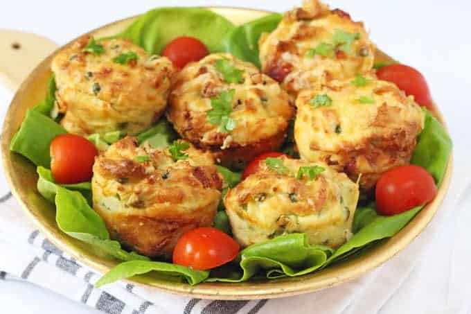 Mashed potato, ham, cheese and pea muffins served on a gold plate, garnished with green leaves and chopped cherry tomatoes