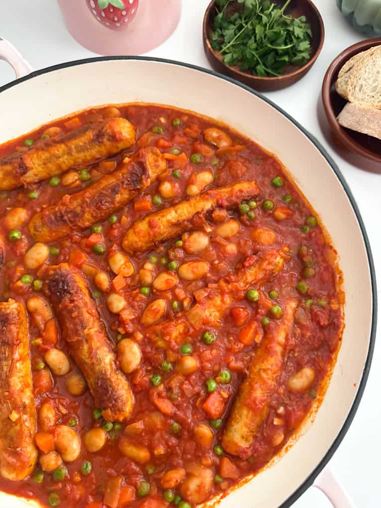 Easy Sausage & Bean Casserole served in a large round cast iron dish next to a side serving of sliced farmhouse bread.