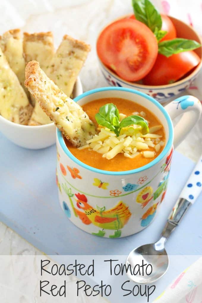 Roasted Tomato Red Pesto Soup served in a colourful mug garnished with a toasted cheese soldier, grated cheese and fresh basil.