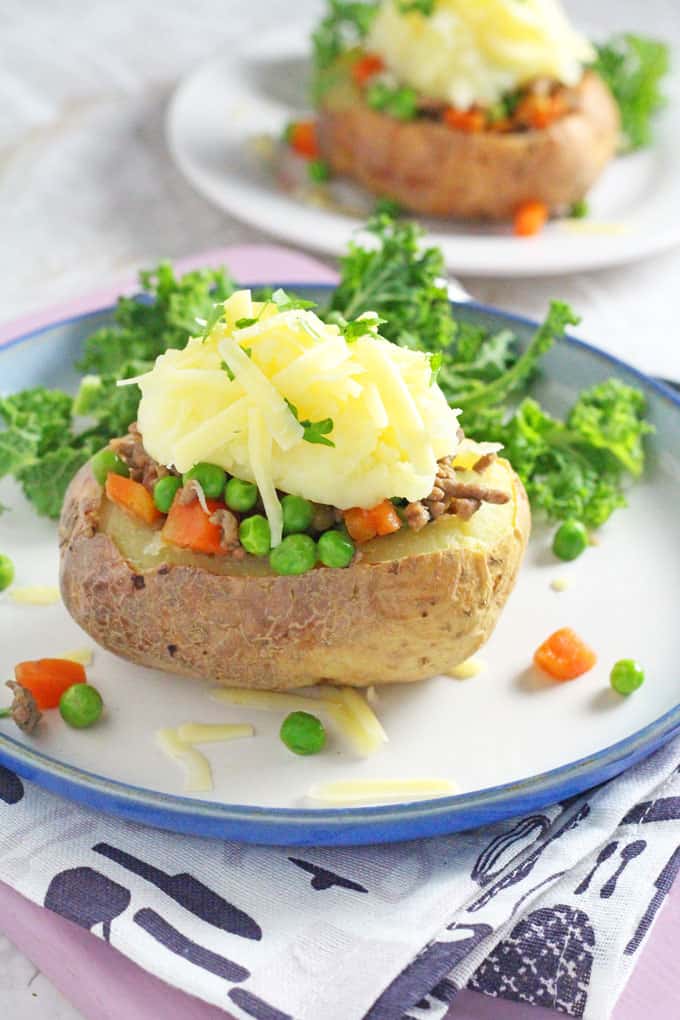 jacket potato boat on a blue and white plate garnished with cheese and greens on the side