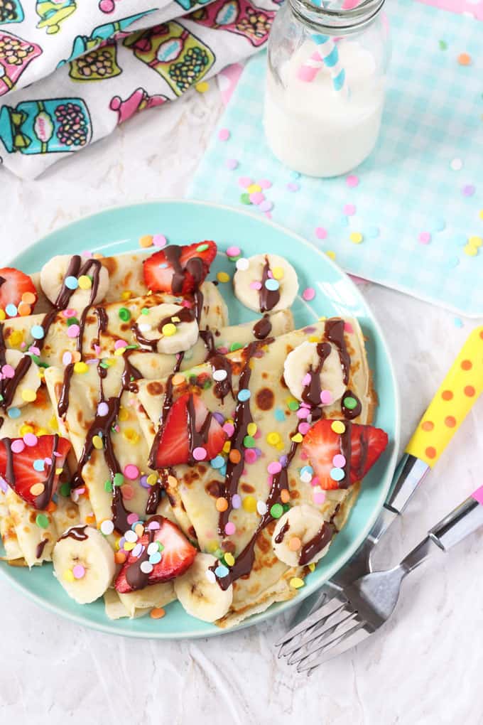 confetti sprinkled pancakes on a blue plate topped with chopped strawberries and chocolate sauce